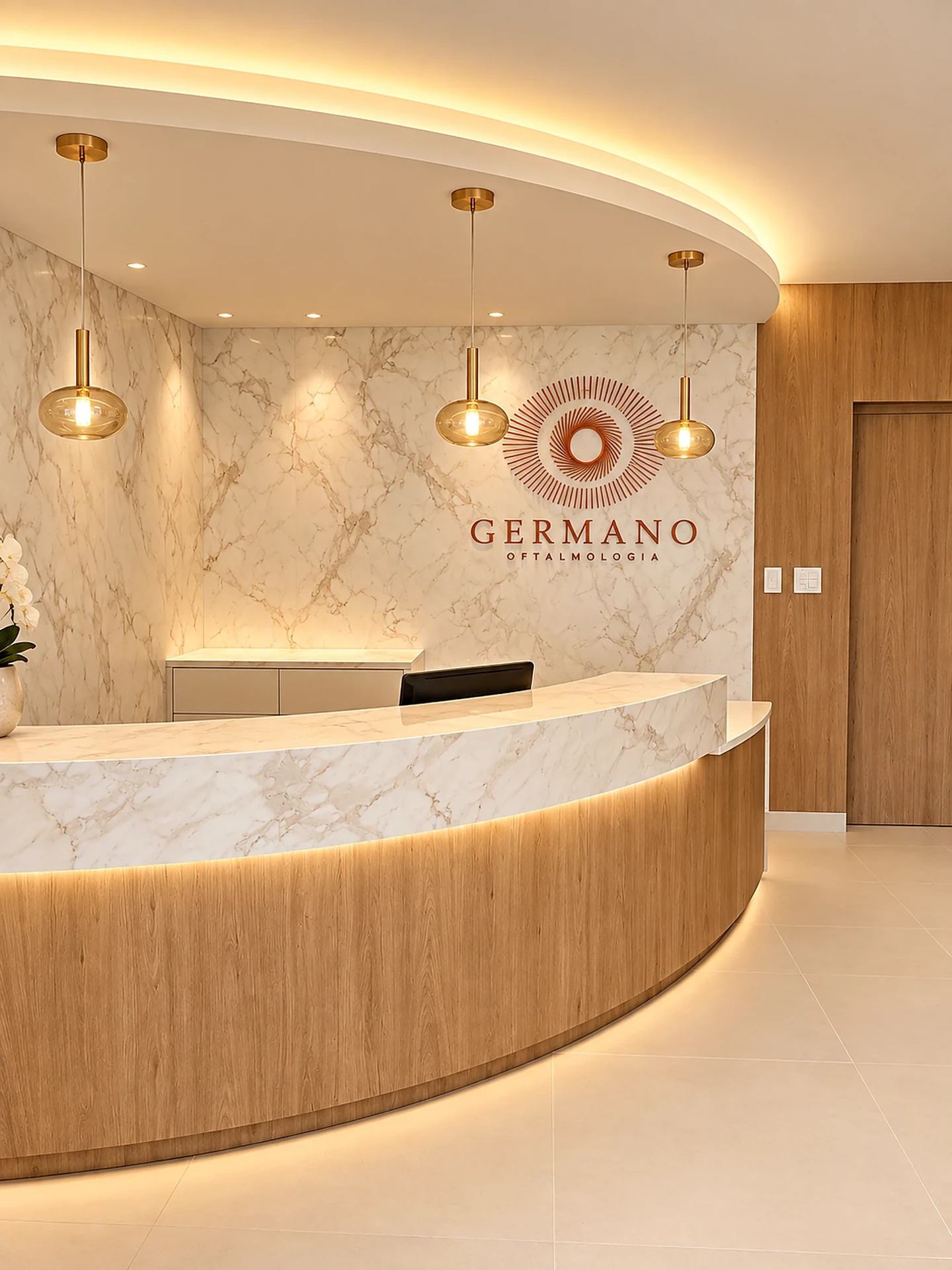 Recepção luxuosa da Germano Oftalmologia em Bauru (SP), com balcão curvo em mármore e madeira, pendentes dourados e logotipo em cobre