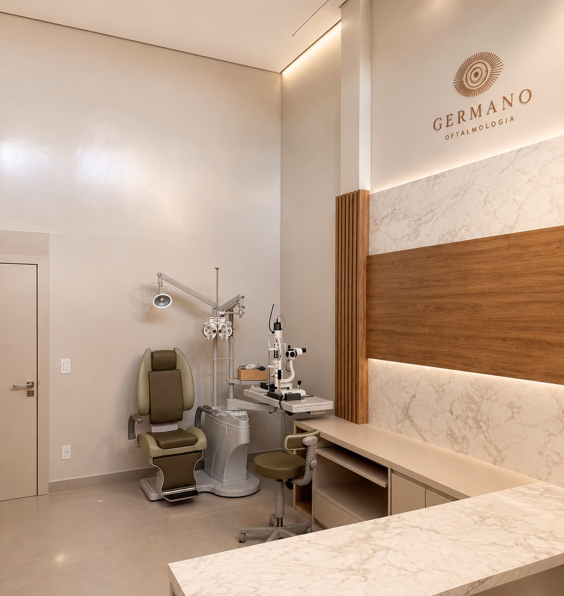 Consultório da Germano Oftalmologia em Bauru, com cadeira de exame, refrator, lâmpada de fenda e bancada em mármore sob o logotipo da clínica